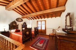 A bedroom with a wooden ceiling, a bed with a red bedspread, a wooden dresser, a chair, and a window with frosted glass. - Tuscan Apartment with Pool & Views (Poppi)