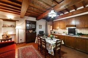 A rustic kitchen with wooden cabinets, a dining table set for four, and a red sofa in the living area. - Tuscan Apartment with Pool & Views (Poppi)