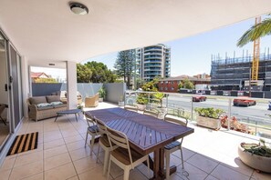 Een balkon met een houten tafel en stoelen, een bank en potten met planten.
