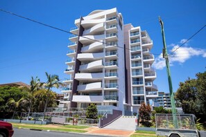 A multi-story hotel with balconies, a clear sky, and palm trees. - Luxury Apartment w/ Pool, Parking, Walk to Beach (Forster)