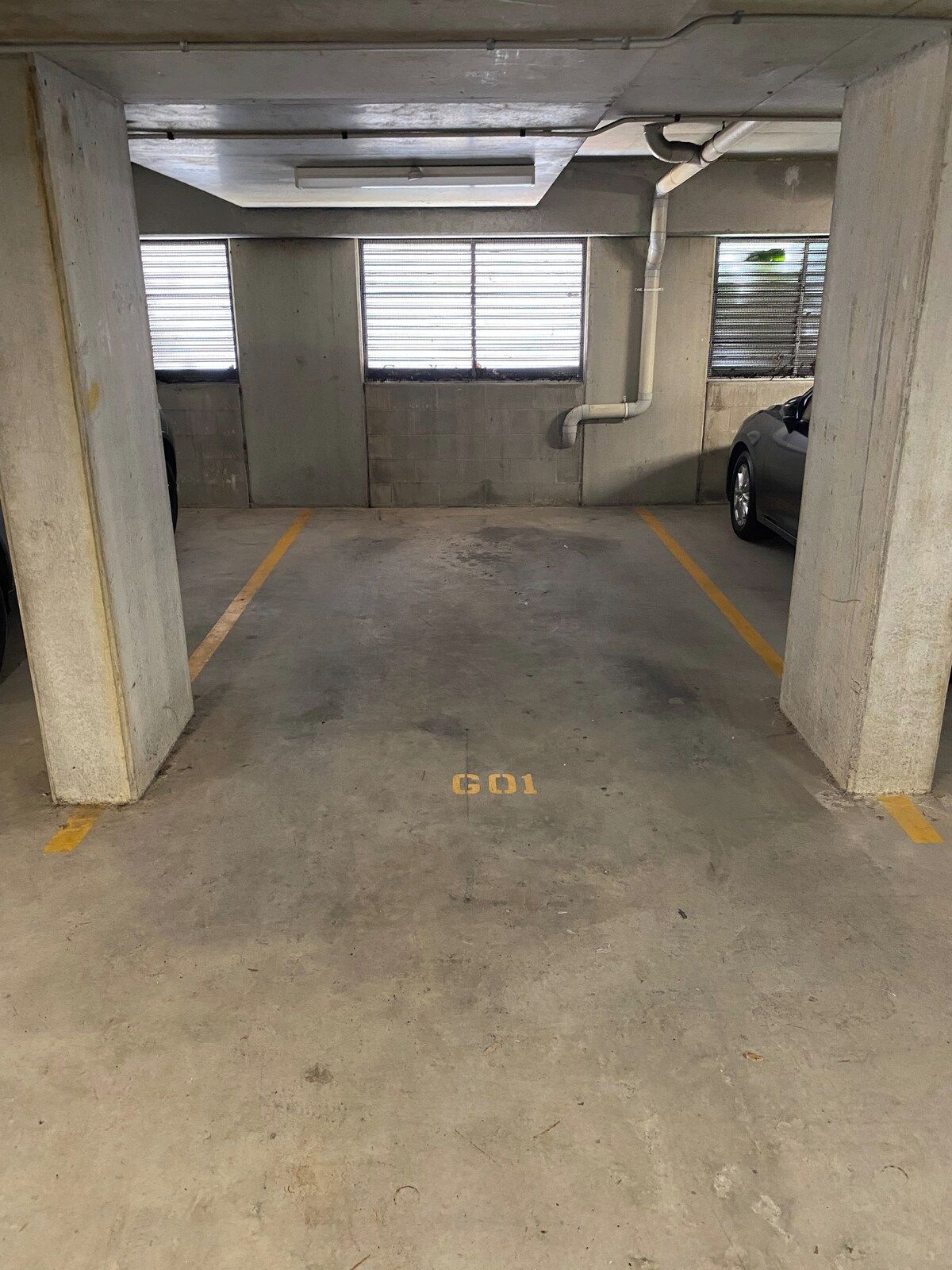 Un garaje de estacionamiento con pilares de concreto, un auto estacionado en un lugar y una marca 'GO1' en el piso.
