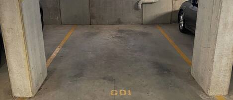 Un garaje de estacionamiento con pilares de concreto, un auto estacionado en un lugar y una marca 'GO1' en el piso.