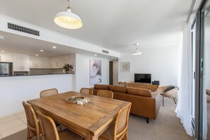 A modern living space with a dining area, a sofa, and a television. - Luxury Apartment w/ Pool, Parking, Walk to Beach (Forster)