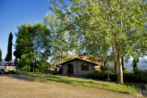 A stone building with a tiled roof, surrounded by trees and a gravel driveway. - Tuscan Apartment with Garden Views (Poppi)