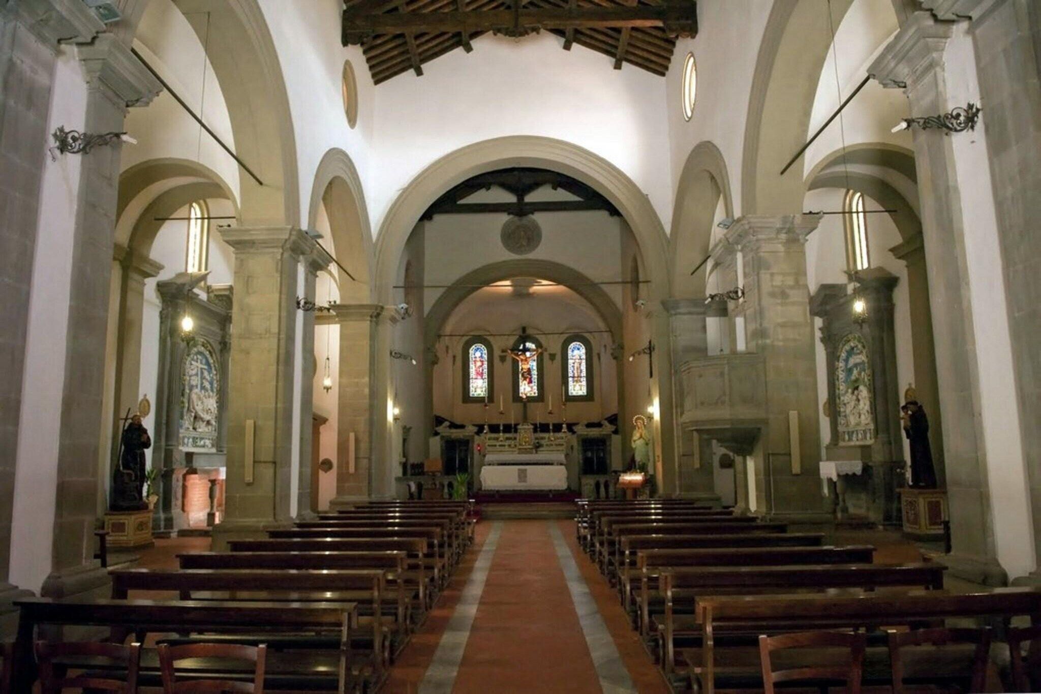 A church interior with arched ceilings, wooden pews, and stained glass windows.
