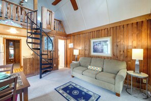 A cozy room with a wooden interior, a sofa, a coffee table, a lamp, a rug, and a spiral staircase. - Flip Flop Cottage: Lake Access in Clermont (Clermont)