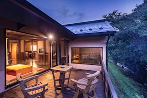 A modern outdoor deck with wooden furniture and a glass enclosure leading to an interior space.