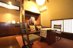 A cozy room with a wooden dining table, two chairs, a sofa, and a built-in closet with hanging clothes.