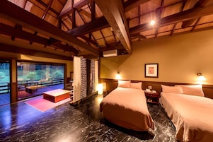 A hotel room with a large bed, a small table, a bench, and a view of the outdoors.
