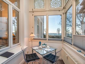 Ein Zimmer mit einem Glastisch, zwei Stühlen, einer Lampe und Meerblick durch große Fenster.