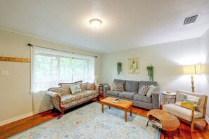 Ein Wohnzimmer mit einem blumengemusterten Sofa, einem grauen Sofa, einem Couchtisch und einem Korbstuhl.