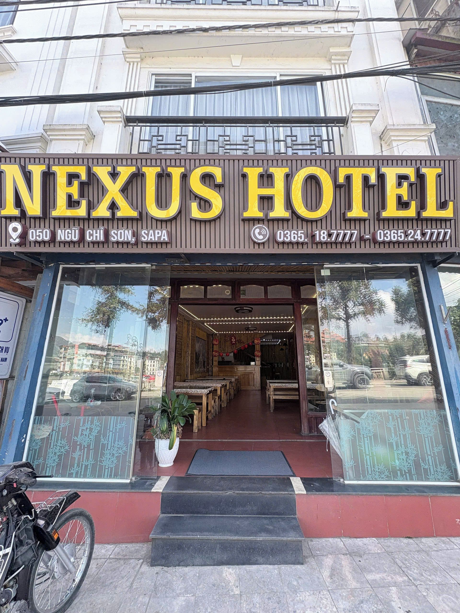 Entrada de un hotel con un letrero que dice 'NEXUS HOTEL' e información de contacto.