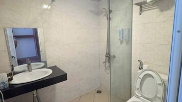 Un baño con ducha de vidrio, lavabo con espejo e inodoro.