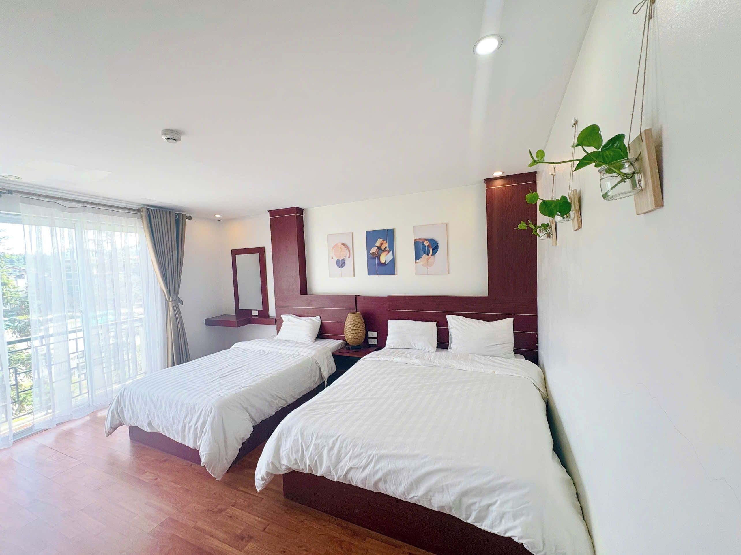 A hotel room with two beds, a large window, and artwork on the wall.