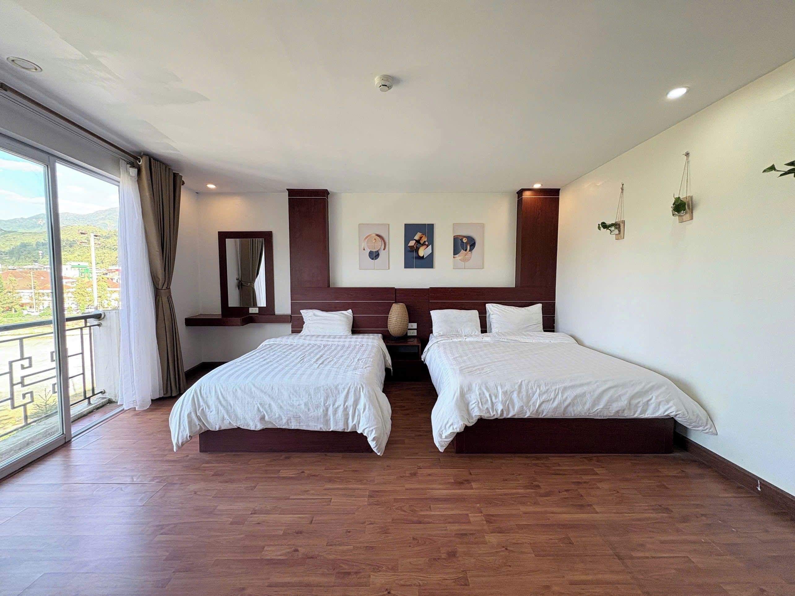 Habitación de hotel con dos camas, un ventanal con cortinas, suelo de madera y vistas al exterior.