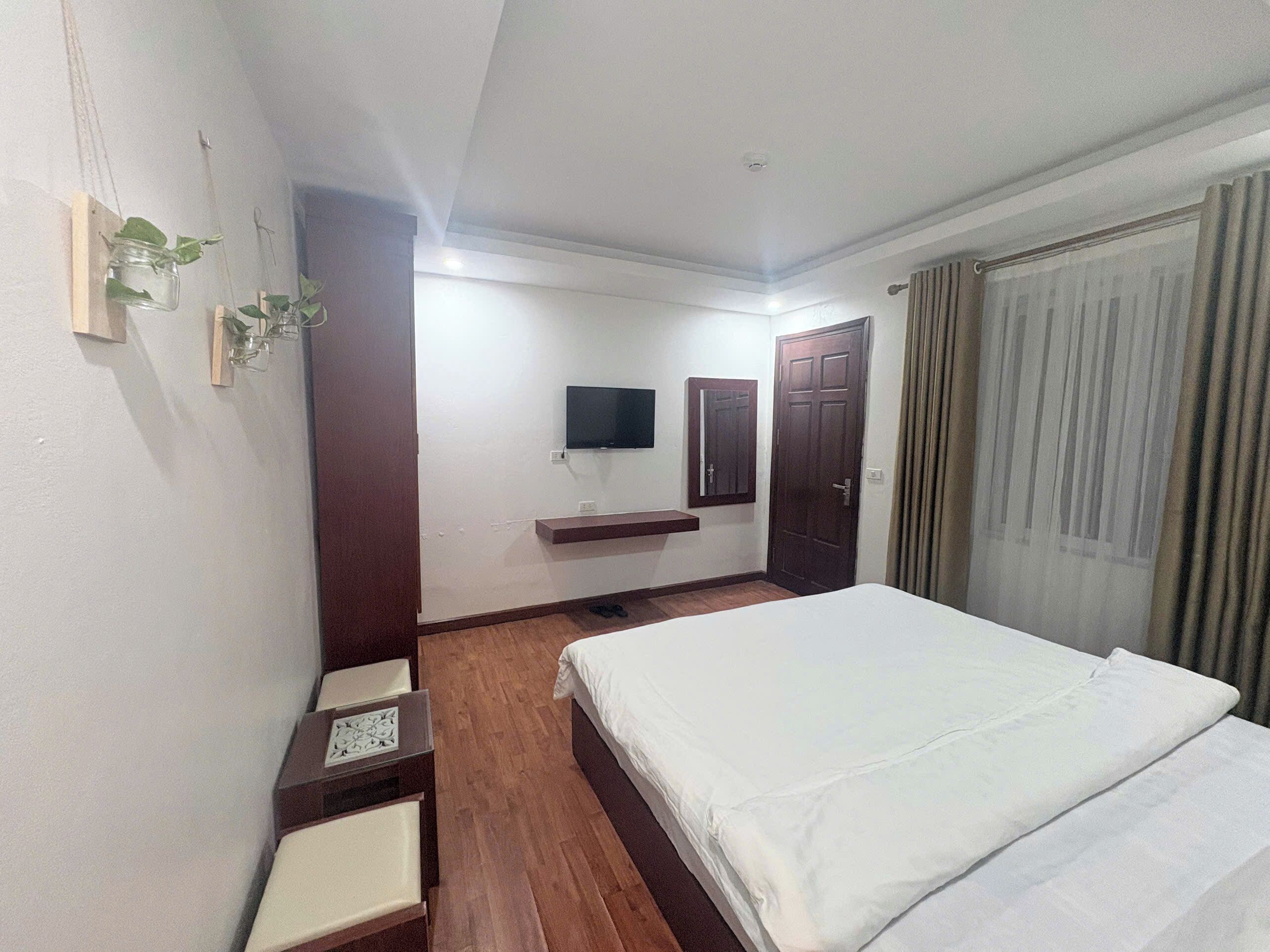A hotel room with a bed, a TV, a wooden nightstand, a mirror, and a door.
