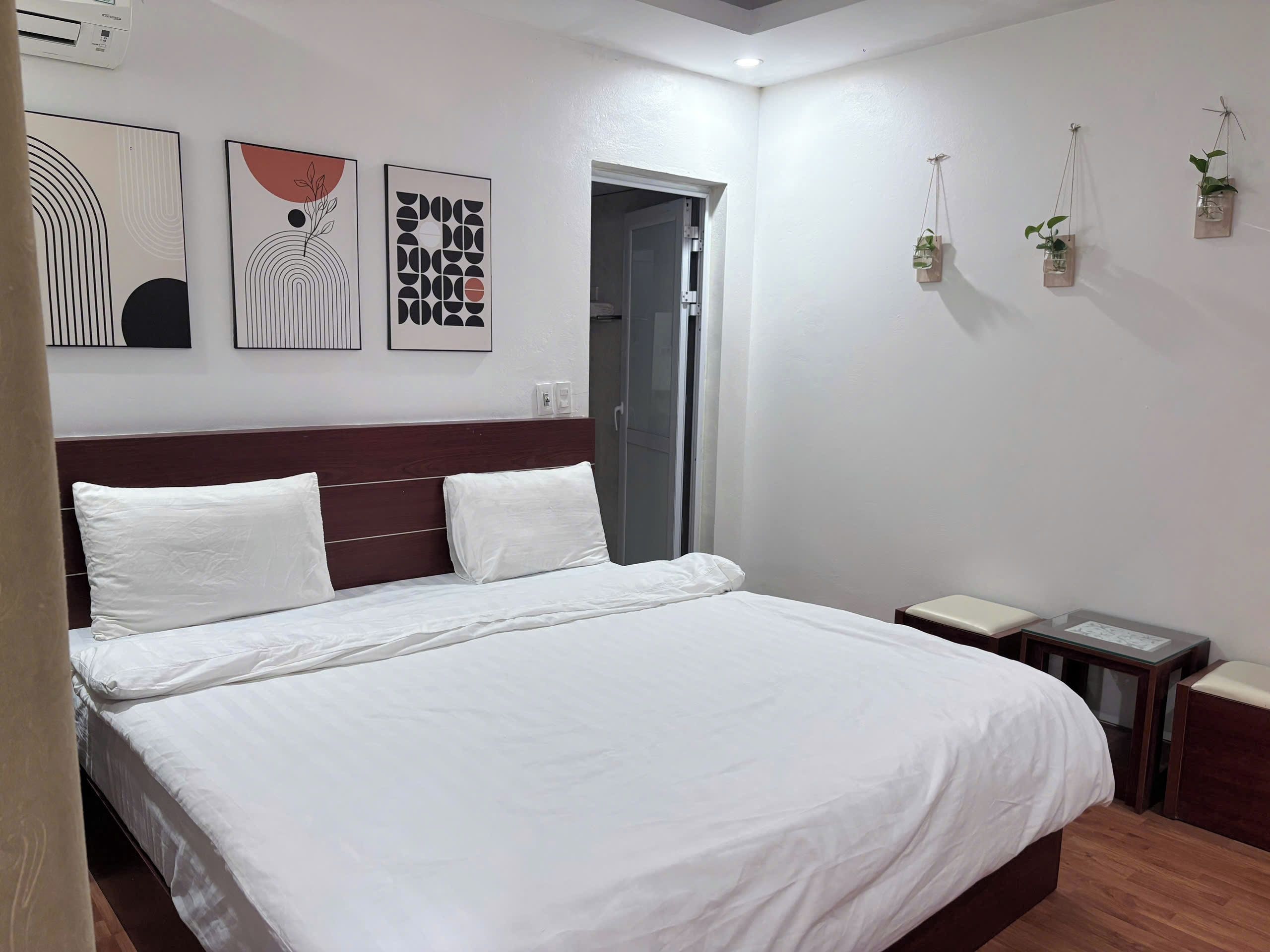 A hotel room with a bed, a wooden headboard, a wall-mounted air conditioner, and two bedside tables.