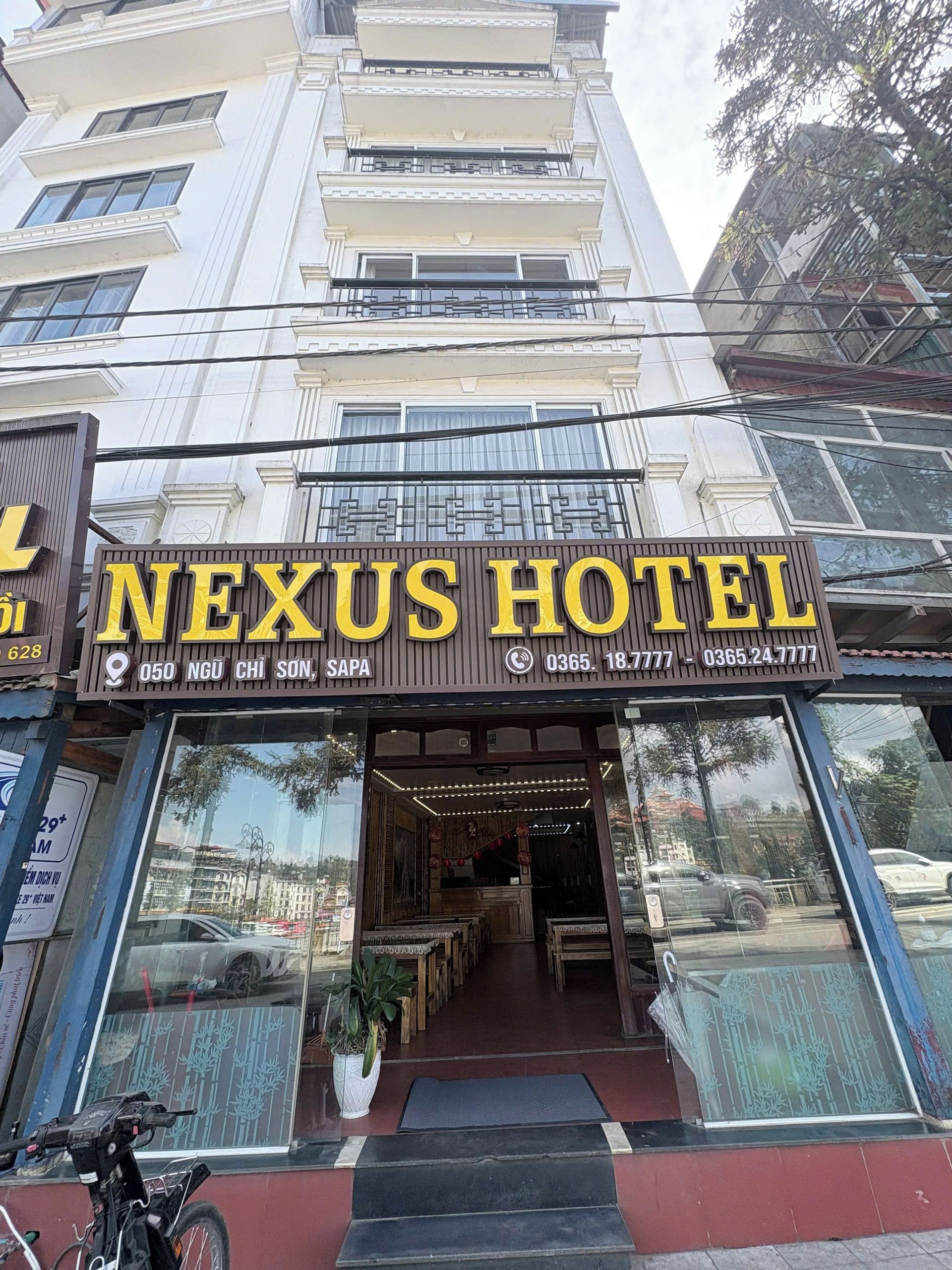 A hotel entrance with a sign reading 'NEXUS HOTEL' and contact numbers.