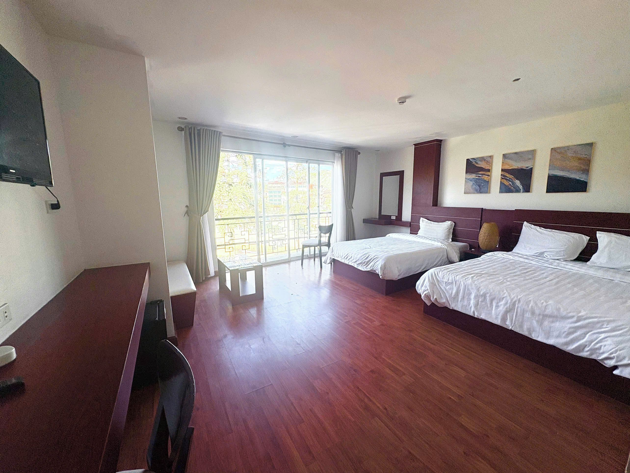 A hotel room with two beds, a desk, a TV, and a large window with curtains.