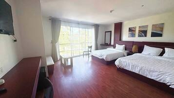 A hotel room with two beds, a desk, a TV, and a large window with curtains.