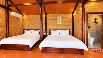 A hotel room with two beds, a brick wall, a wooden ceiling, and a bathroom visible through an open door.