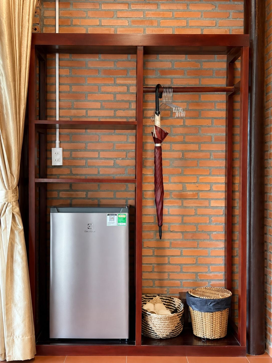 A compact room with a brick wall, a built-in refrigerator, a hanging umbrella, and two baskets.