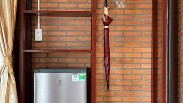 A compact room with a brick wall, a built-in refrigerator, a hanging umbrella, and two baskets.