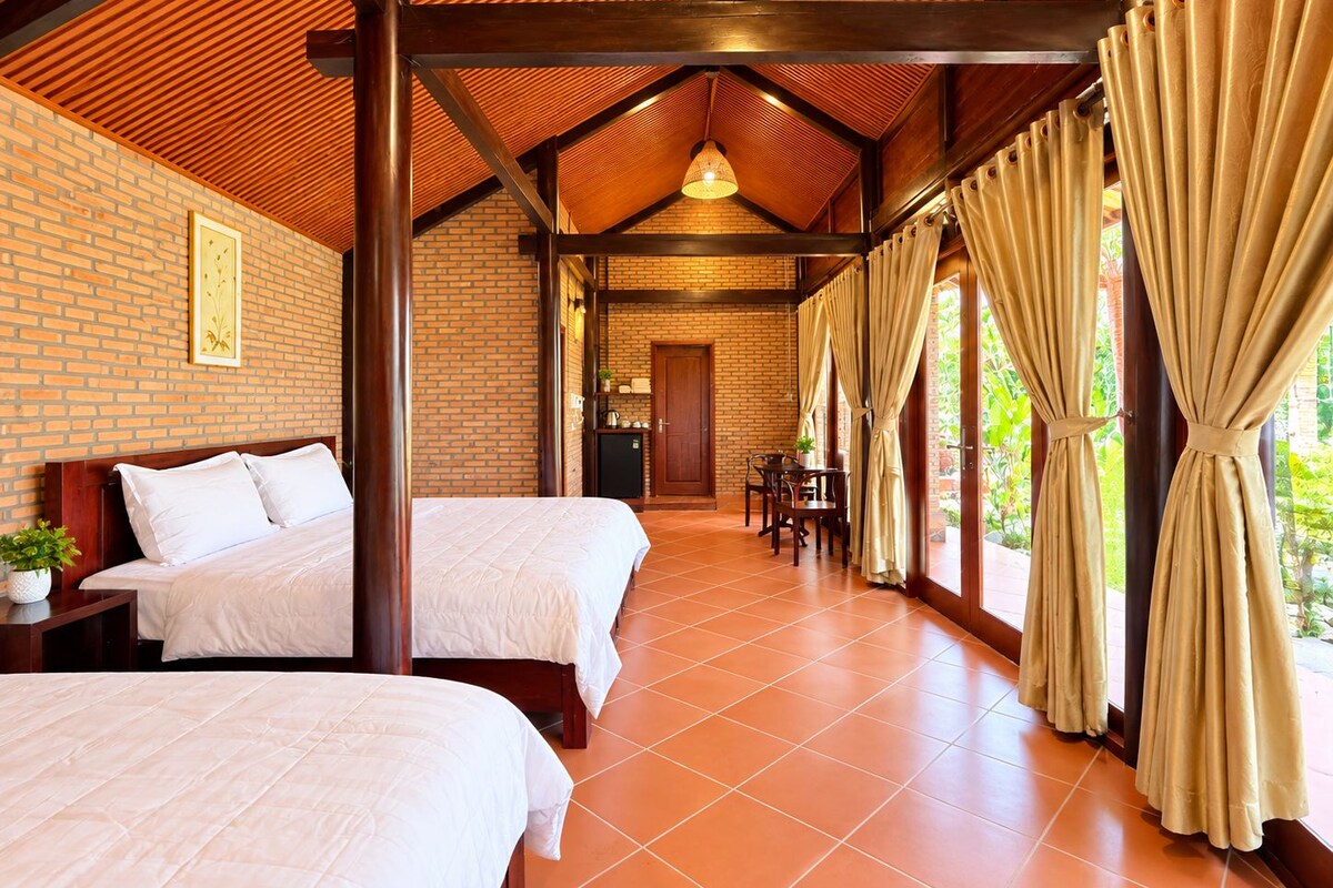 Quarto de hotel com duas camas, área de refeições e cozinha visível através de uma porta aberta.