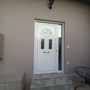 Eine weiße Tür mit Fensterglas, ein kleiner Podeststufenaufgang davor und eine Wandleuchte darüber.