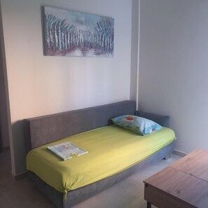 Ein Einzelbett mit grüner Bettdecke und Kopfkissen, ein Nachttisch aus Holz und ein Bild an der Wand.