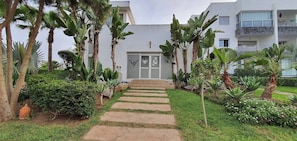 A pathway leading to a building with a white facade, surrounded by tropical plants and a clear sky. - 3 Bedrooms Pools Terrace Beach Dar Bouazza (Dar Bouazza)