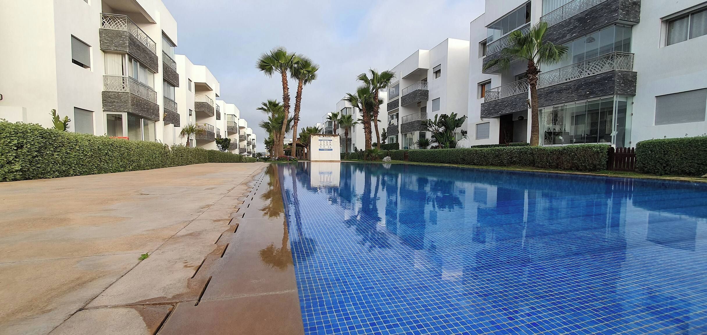 Ein Pool mit gefliestem Rand, umgeben von modernen Gebäuden mit Balkonen und Palmen.