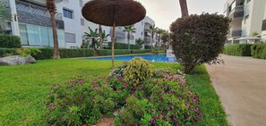 Un jardin bien entretenu, doté d’une piscine, de palmiers et d’un parasol en chaume.