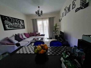 A living room with a sofa, a coffee table with fruit, a TV, and a wall with 'HOME' decor. - Sunshine & Smiles – Nabq’s Most Lovely Apartment (South Sinai Governorate)