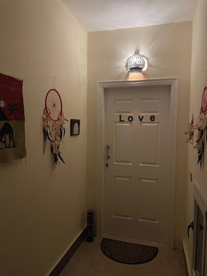 Ein Flur mit einer weißen Tür mit der Aufschrift 'Love', einem Traumfänger und einem kleinen Teppich.