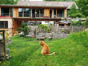 A wooden house with a balcony, a fenced backyard, and a cat sitting on the grass. - Holiday Apartment With 1 Bedroom (Bad Toelz)