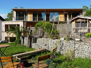 A modern wooden house with a balcony, stone wall, and outdoor seating area. - Holiday Apartment With 1 Bedroom (Bad Toelz)