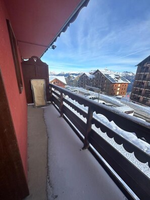 Un balcon doté d’une rambarde en métal, donnant sur une ville de montagne enneigée avec ses bâtiments.