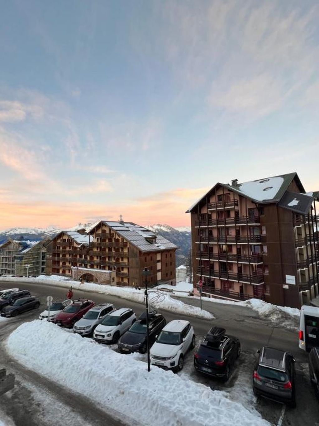 Een hotel met meerdere verdiepingen, een parkeerplaats met auto's en sneeuw op de grond.