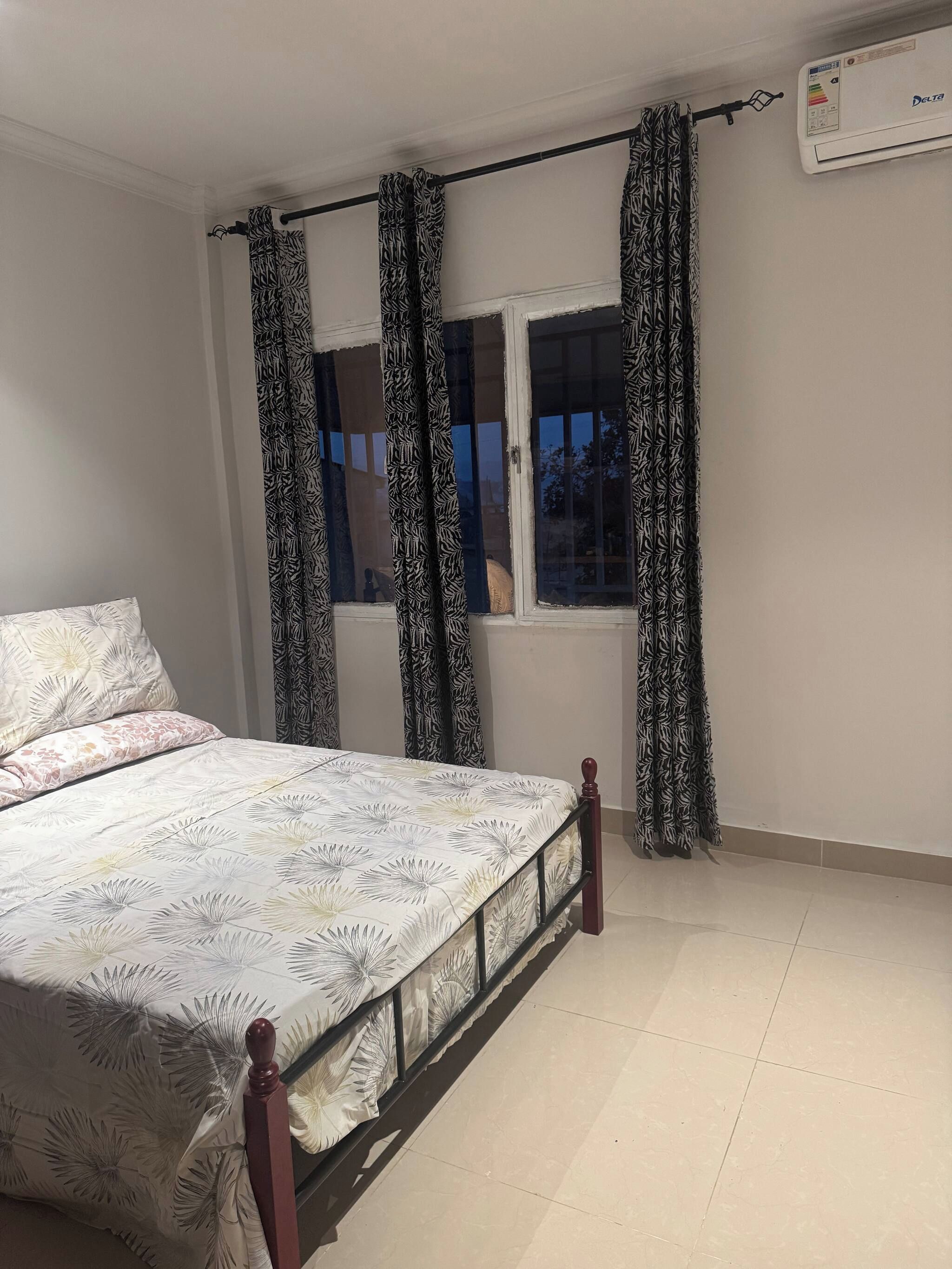 A bedroom with a bed, curtains, a window, and an air conditioning unit.