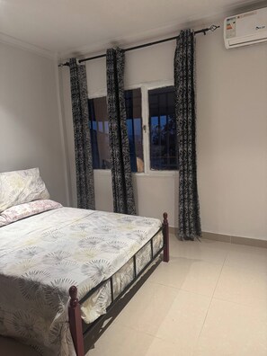 A bedroom with a bed, curtains, a window, and an air conditioning unit.