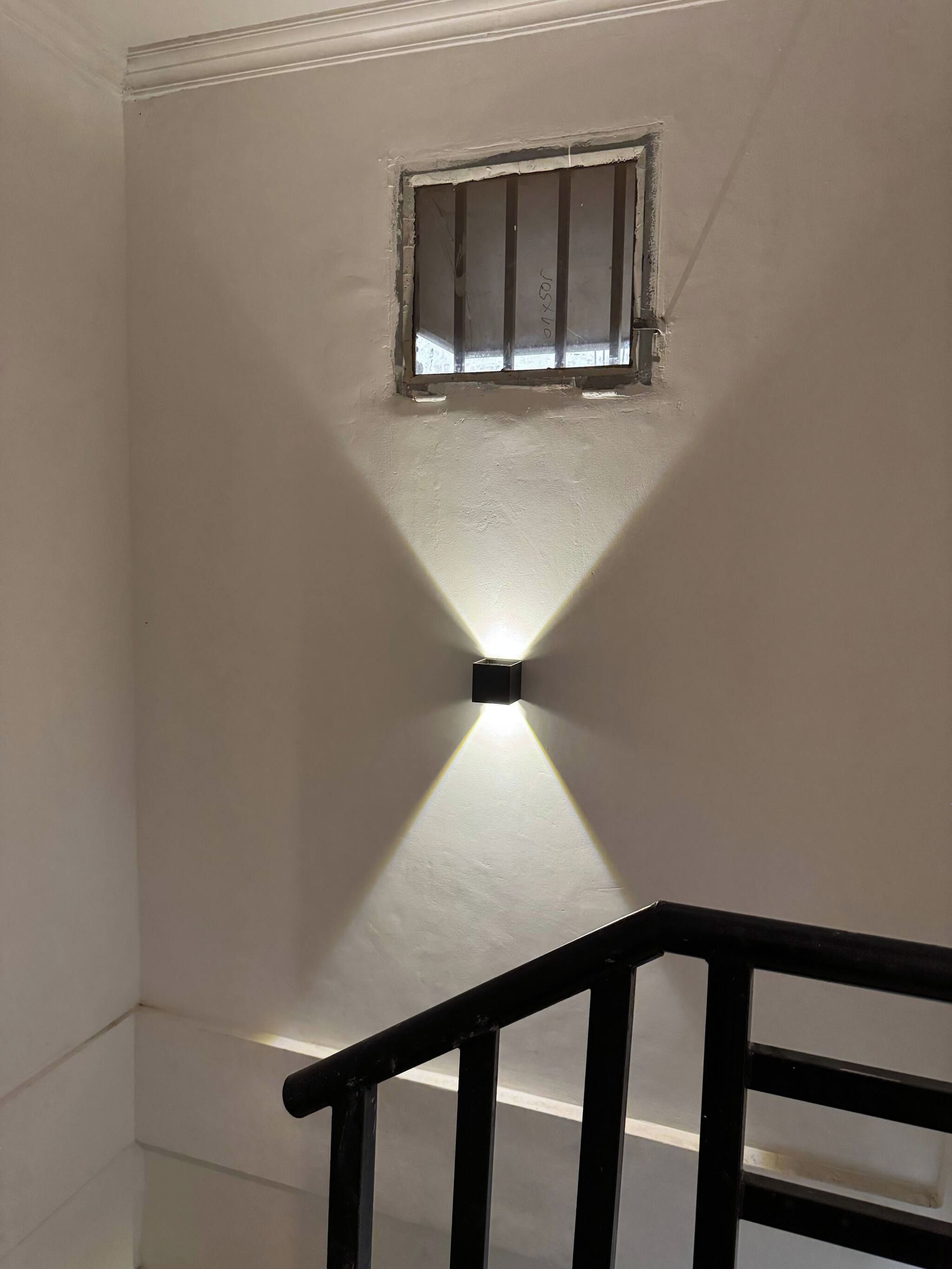 A staircase with a handrail and a wall-mounted light fixture casting a shadow.