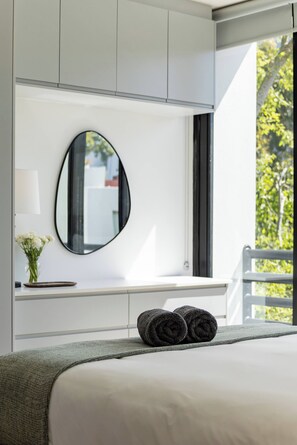 A modern bedroom with a large bed, a round mirror, and a view of greenery outside. - Modern luxury Claremont apartment - sleeps 6 (Cape Town)