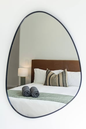 A bed with pillows and rolled towels, a bedside lamp, and a wall-mounted mirror. - Modern luxury Claremont apartment - sleeps 6 (Cape Town)