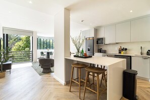 A modern kitchen with a large island, bar stools, and a view of the outdoors. - Modern luxury Claremont apartment - sleeps 6 (Cape Town)