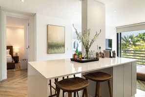 A modern kitchen with a central island, bar stools, a large window with a view of greenery, and a painting on the wall. - Modern luxury Claremont apartment - sleeps 6 (Cape Town)