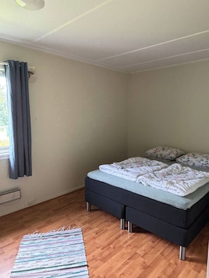 Ein Schlafzimmer mit einem Bett, einem Fenster mit Vorhängen, einem Heizkörper und einem Holzboden.