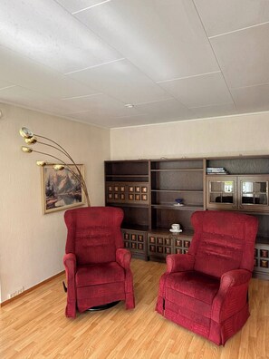 Ein Zimmer mit zwei roten Sesseln, einem Holzschrank mit Glastüren und einem Bild an der Wand.