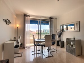 A modern dining area with a table and chairs, a lamp, and a view of buildings through a large window. - Beautiful 2 bedroom terrace and parking (Cannes)