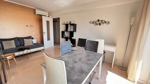 A modern living room with a sofa, a dining table with chairs, a bookshelf, and an air conditioning unit. - Beautiful 2 bedroom terrace and parking (Cannes)